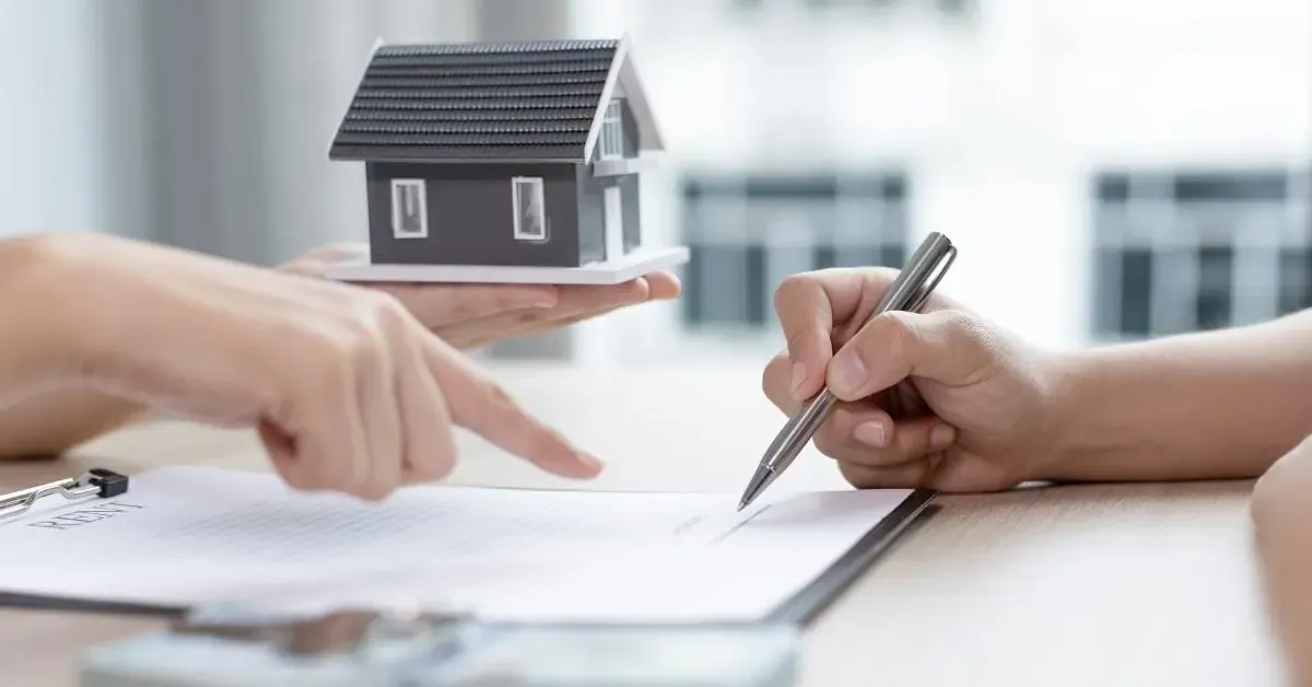 One hand signing a paper and another hand handing out a house figurine 